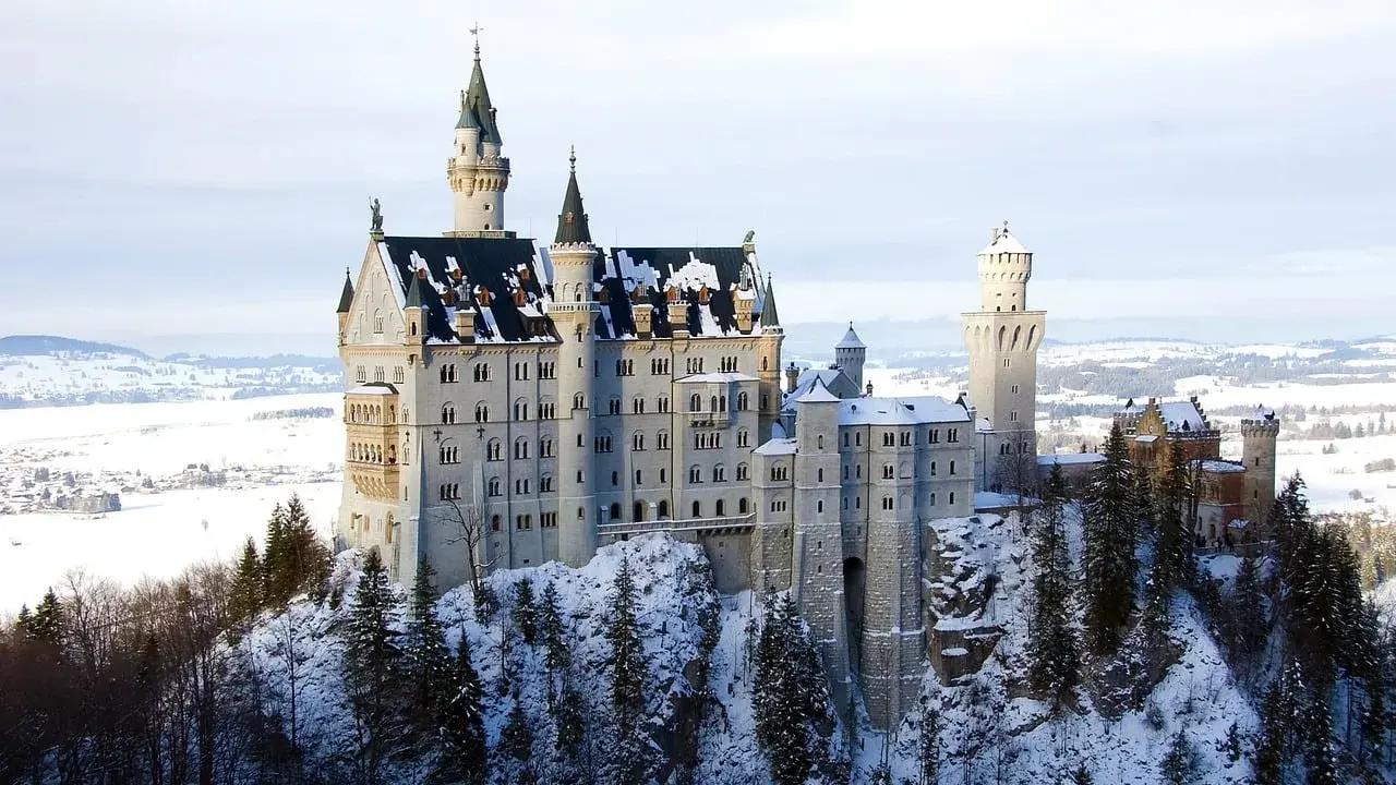 Zamek Neuschwanstein w zimowej scenerii, otoczony ośnieżonymi drzewami i krajobrazem.