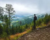 Mężczyzna z plecakiem podziwia widok na gęsto zalesione góry. To prawdziwy hiking po polsku, z mgłą otulającą szczyty.