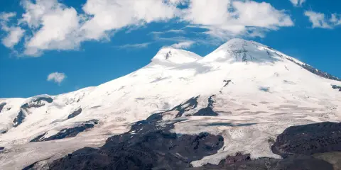 Elbrus, najwyższy szczyt Rosji, wznosi się dumnie pod błękitnym niebem z kłębiastymi chmurami. Lodowce spływają po jego zboczach.