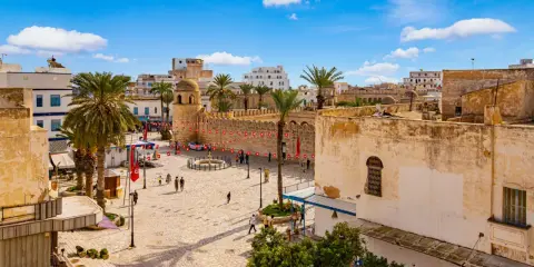 Tunezja Sousse czy warto? Rynek z palmami, zabytkową wieżą i flagami. Słoneczny dzień zachęca do zwiedzania.