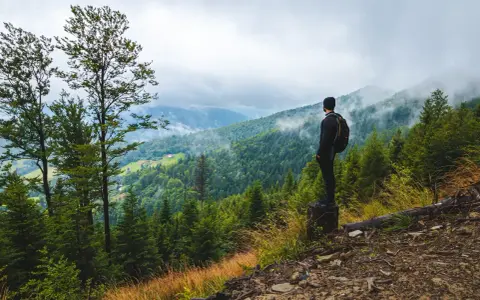 Mężczyzna z plecakiem podziwia widok na gęsto zalesione góry. To prawdziwy hiking po polsku, z mgłą otulającą szczyty.