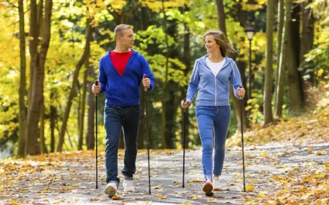 Para spaceruje po jesiennym parku, ciesząc się chodzeniem z kijkami wśród kolorowych liści.