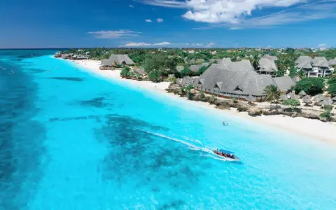 Idealna pogoda na Zanzibarze w czerwcu: turkusowa woda, biała plaża i łódź z turystami.