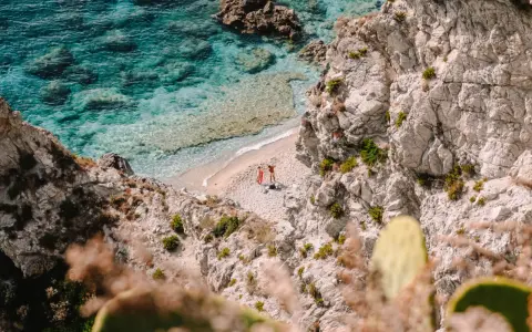 Malownicza zatoczka na Kalabrii, gdzie warto zobaczyć turkusowe morze i skaliste wybrzeże. Dwie osoby odpoczywają na piaszczystej plaży.
