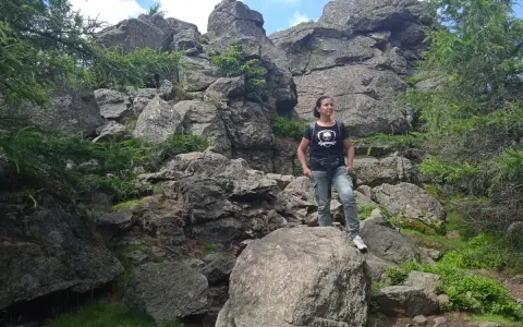 Kobieta na szlaku Wysoka Kopa, otoczona skalnymi formacjami i zielenią.