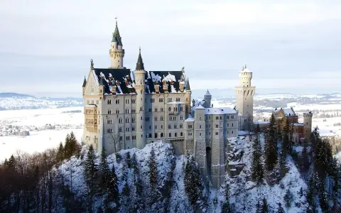 Zamek Neuschwanstein w zimowej scenerii, otoczony ośnieżonymi drzewami i krajobrazem.
