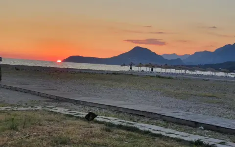 Zachód słońca nad morzem w Czarnogórze w czerwcu. Idealna pogoda na plażowanie, z górami w tle i rzędem parasoli.