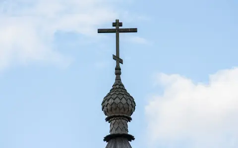 Drewniany krzyż na kopule cerkwi, symbol religii w Gruzji, na tle błękitnego nieba z chmurami.
