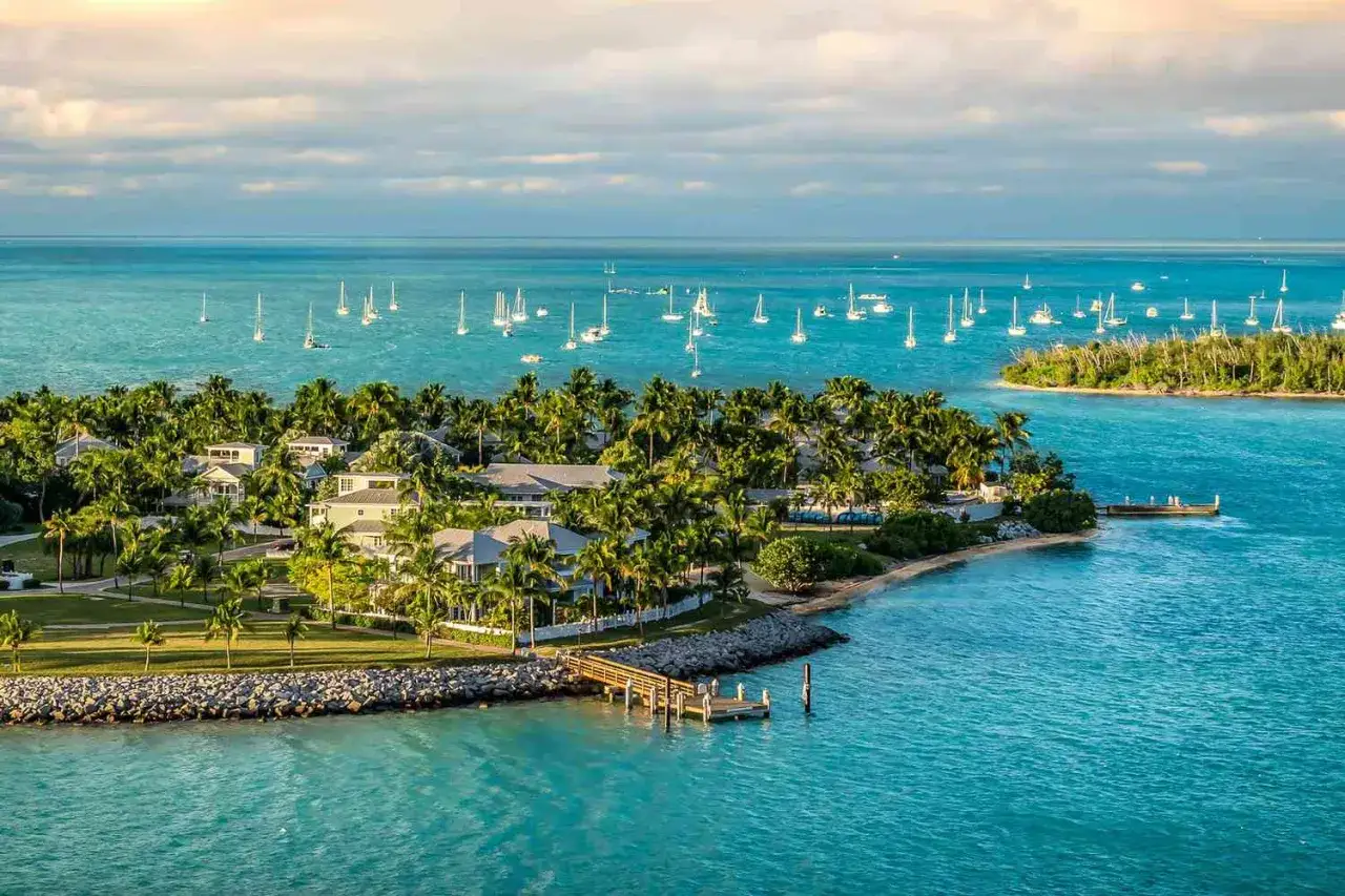 Rajska wyspa z palmami i domkami, gdzie jest ciepło w grudniu i tanio. Wiele żaglówek na turkusowym morzu.