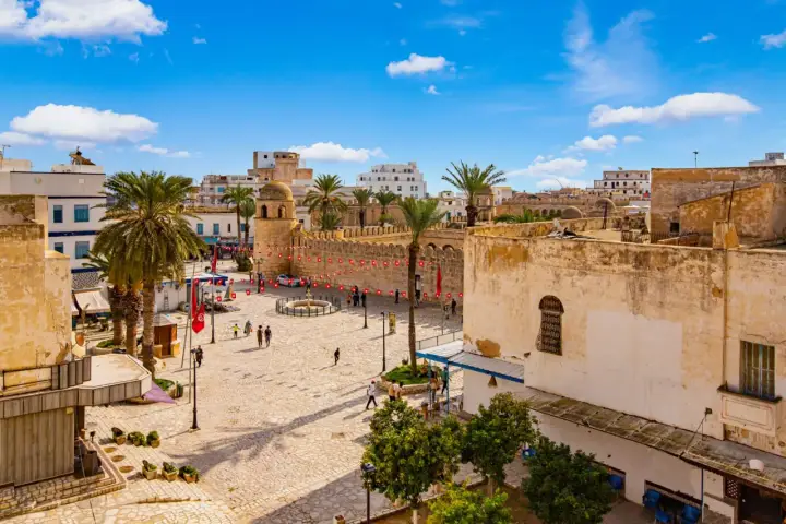 Tunezja Sousse czy warto? Rynek z palmami, zabytkową wieżą i flagami. Słoneczny dzień zachęca do zwiedzania.